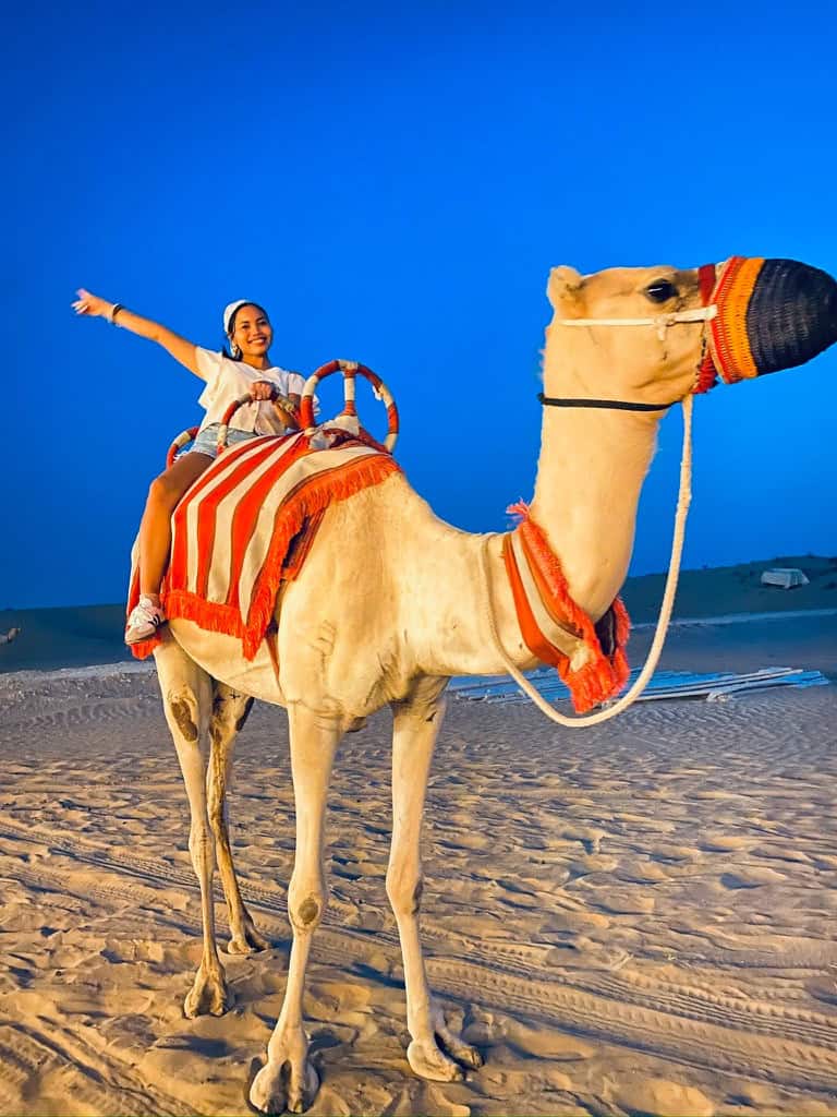 Dopegine riding a camel on sandy ground at dusk.
